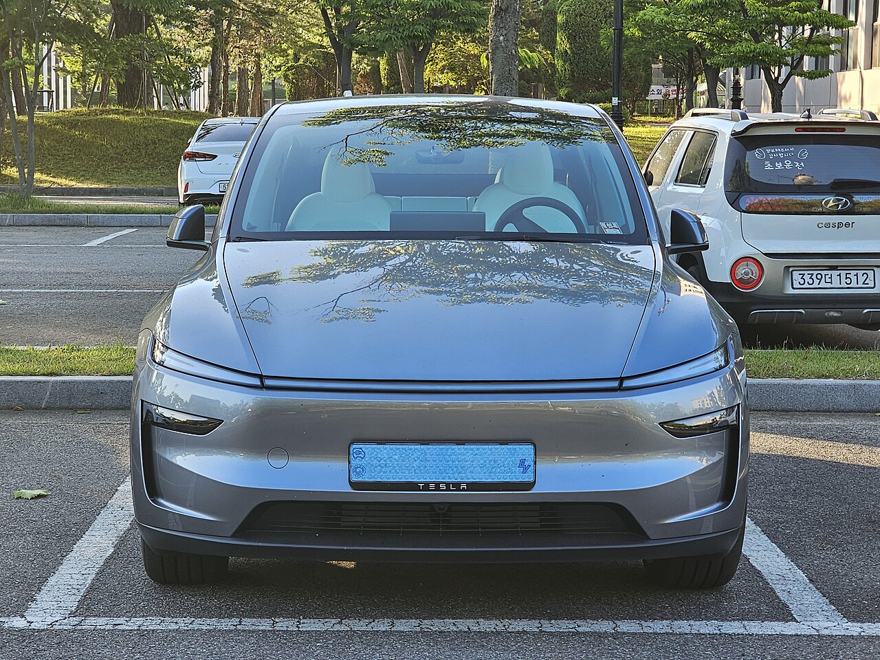Tesla Model Y รุ่นปรับโฉมสีเทาเงิน มุมด้านหน้าตรง จอดในลานจอดรถ