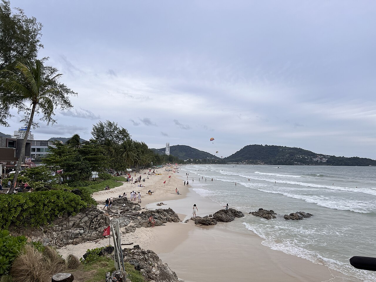 หาดป่าตอง ภูเก็ต มองจากฝั่งเหนือ มีธงแดงปักริมหาดและร่มร่อนเหนืออ่าว